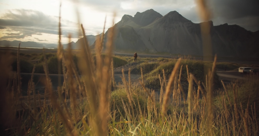 Wanderer stands in the distance on a black-sanded dune and spreads his arms in a grassy mountain landscape