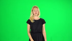 Girl tourist goes and takes a selfie, then looks through the photos on the smartphone. Blonde female dressed in black dress isolated on green screen at studio.