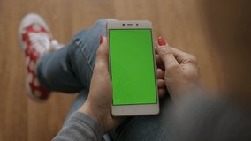 Girl Using Touchscreen Mobile Phone. Young Woman Home Sitting on a Chair with Green Screen Smartphone in Vertical Mode. Girl Using Smartphone, Browsing Internet, Watching Video Content, Blogs. POV.