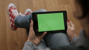 Girl Using Touchscreen Mobile Tablet. Young Woman Home Sitting on a Chair with Green Screen Tablet in Horizontal Mode. Girl Using Smartphone, Browsing Internet, Watching Video Content, Blogs. POV.