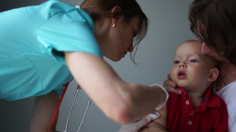 Woman pediatrician gives a flu shot to a baby sitting in the arms of a mother. Close-up. Insulin Injection, Routine Vaccination