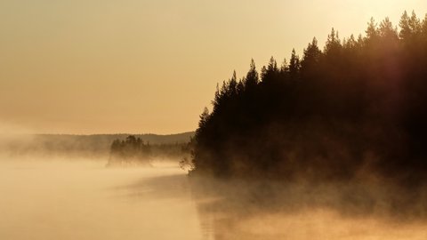 Morning fog on the lake at sunrise. Misty landscape with small island on the lake.