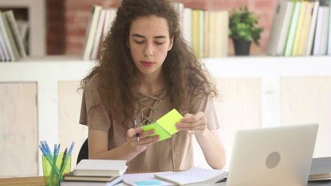Teenager girl sitting in library or classroom writing noting using sticky notes clever responsible absorbed student female prepare for university session, learn study process essay creation concept