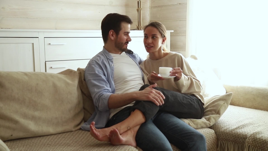 Girlfriend holds cup drinks tea or coffee sit close to boyfriend resting together on couch talking plan day future life or vacation enjoy free weekend day, romantic relations activity at home concept