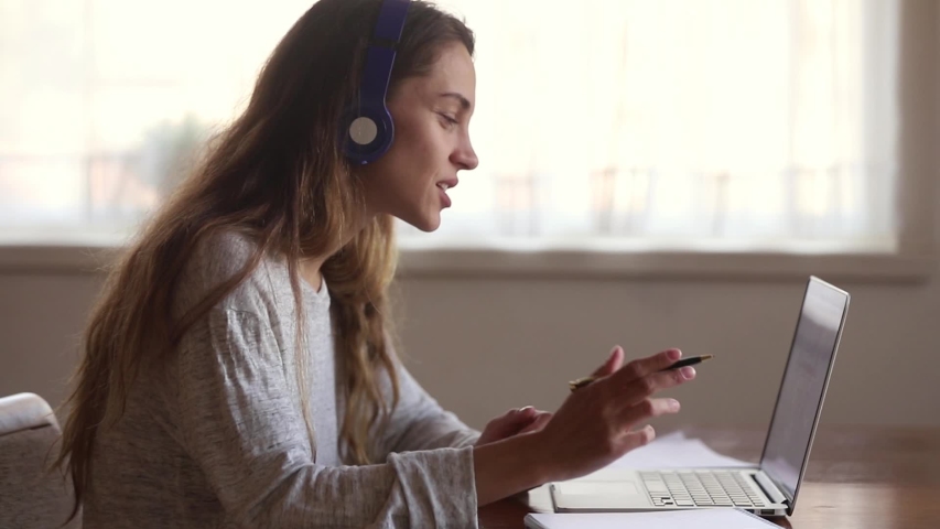 Girl sit at desk in headphones makes video call talks with teacher improve language skills learns online, entrepreneur translator interact with client look at pc screen chatting noting working at home Royalty-Free Stock Footage #1038796313