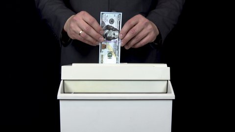 Schroeder destroys one hundred dollar bill. Businessman in a suit thrusts money into a paper shredder