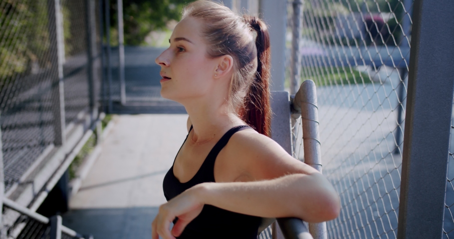 Close up of cute healthy young female leaning on metal fence and smiling looking to camera, leisure summer morning of happy nice girl resting outdoor after power workout and physical activity Royalty-Free Stock Footage #1038797411