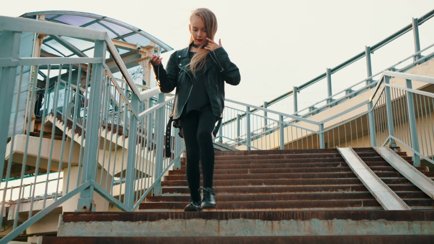 Teenager girl in black leather jacket walking down stairs on urban background. Rock girl in leather jacket going down on staircase bottom view