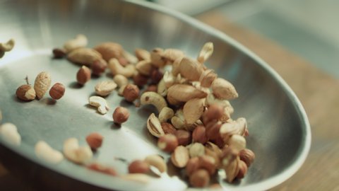 Closeup mix of nuts tossing on frying pan in slow motion. Closeup hazel nuts frying on metal pan. Close up hazel and cashew nuts roasting in slow motion.