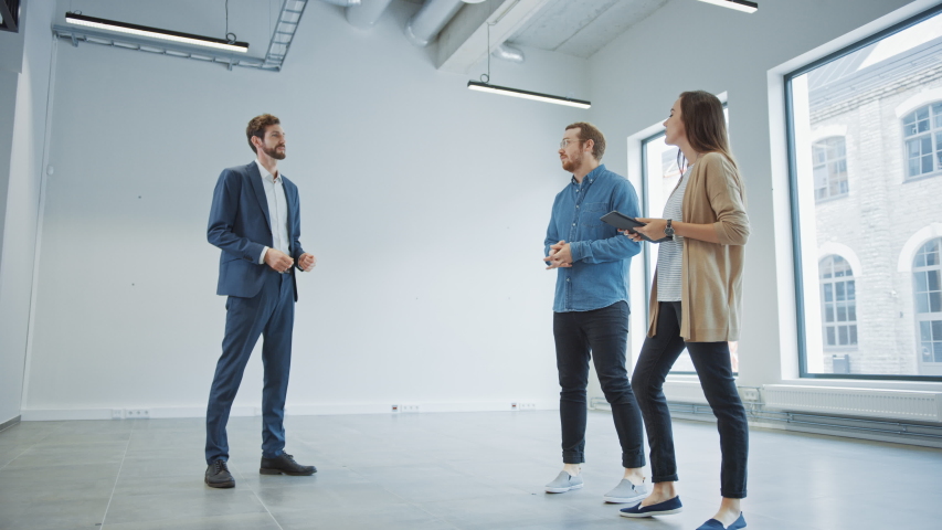 Real Estate Agent Showing a New Empty Office Space to Young Male and Female Hipsters. Entrepreneurs Meet the Broker with a Tablet and Discuss the Facility They Wish to Purchase or Rent. | Shutterstock HD Video #1038801305