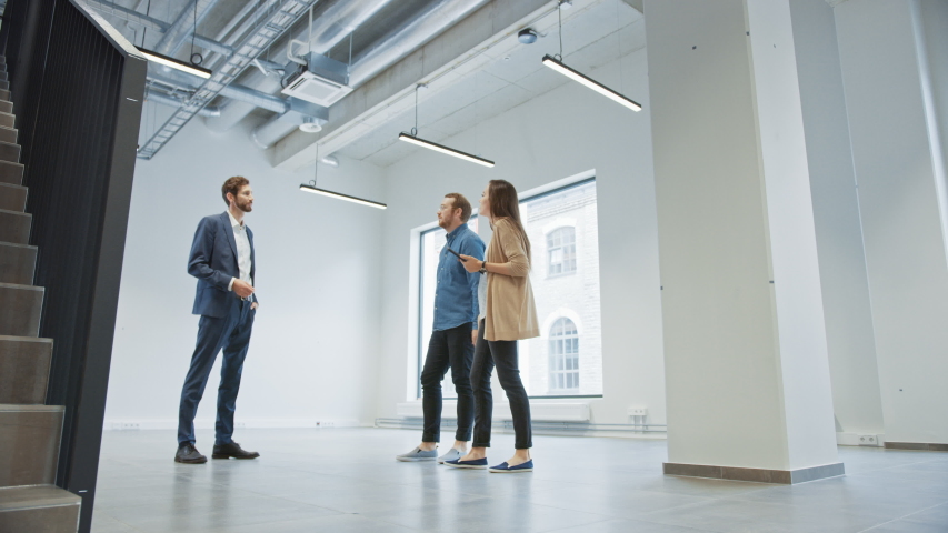 Real Estate Agent Showing a New Empty Office Space to Young Male and Female Hipsters. Entrepreneurs Meet the Broker with a Tablet and Discuss the Facility They Wish to Purchase or Rent.