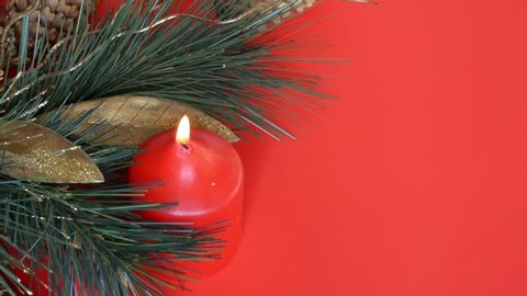 Christmas decorations - burning flame of a New Year's red candle. Fir branches with balls, cones and red candle in red background with a Christmas branch.