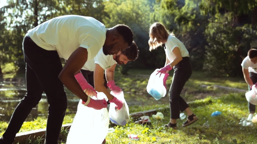 Young team of environmental volunteers picking up garbage into plastic bags and clearing polluted city park in sunny weather. Save nature. Concept of ecology. Royalty-Free Stock Footage #1038801839