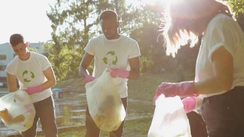 Team of young nature activists wearing eco T-shirts picking up plastic garbage cleaning down the public park on sunny day. People save environment. Concept of ecology. | Shutterstock HD Video #1038801881