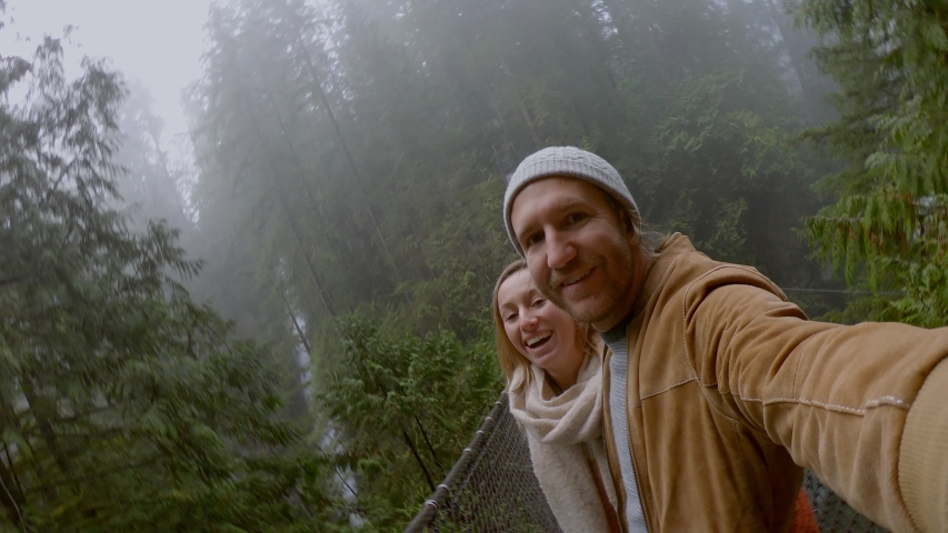 Young couple hiking in pristine forest take cool selfie on a suspended bridge. Canada  Royalty-Free Stock Footage #1038805457