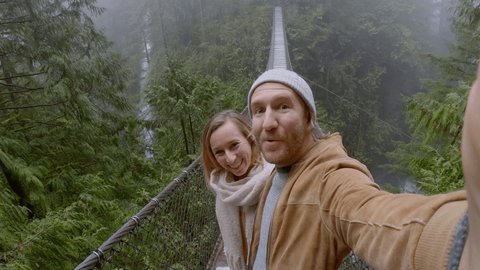 Young couple hiking in pristine forest take cool selfie on a suspended bridge. Canada 