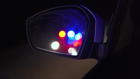 Flashing police lights reflected in the rearview mirror of a car at night