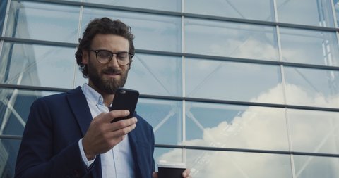 Handsome bearded Startup Businessman in Glasses using mobile Phone. Young man texting Messages, cheating on his Smartphone while walking in Office District. Business. Social Networking. People. Apps.