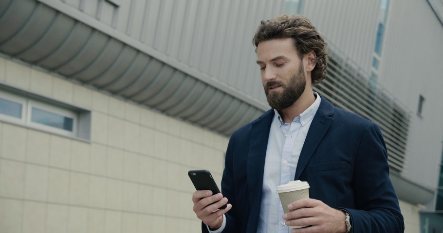  Businessman  texting Messages on his Smartphone and smile.  Man walking near modern Office Building and holding a cup of Coffee Royalty-Free Stock Footage #1038809960