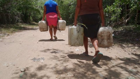 Women in Honduras cary heavy water jugs on a dirt road.