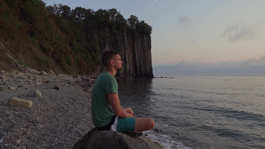 A man at sunset sits on a rock and enjoys the sea and nature. Portrait of a man at sunset, rocks and sea in the background