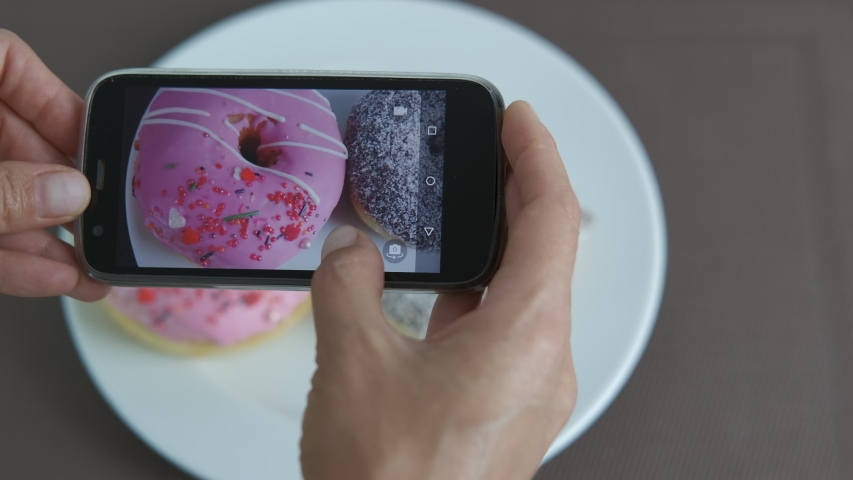 Sweets on telephone. Female with a telephone make a photo of two glases doughnut on the plate.