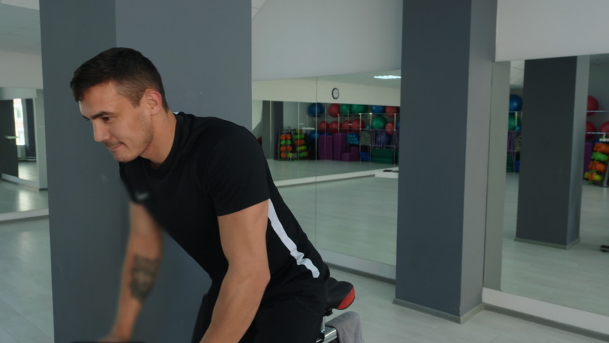 Athletic young man cycling on bike in gym. Muscular young man in sportswear training on exercise bike in gym