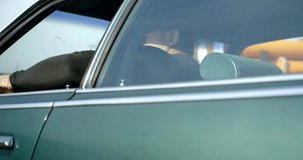 brutal man is sitting inside old rarity car in sunny day, adjusting rearview mirror by hand