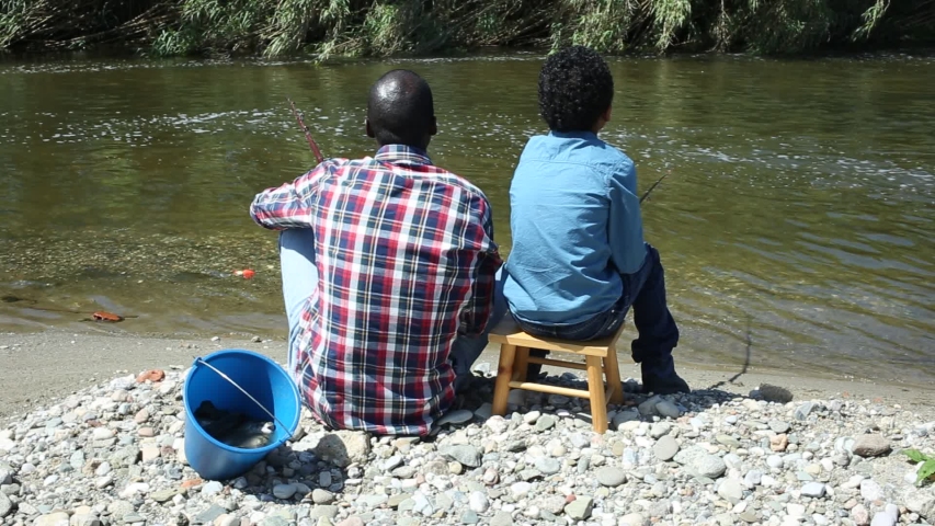 Back portrait of little boy and his father fishing with rods on river

