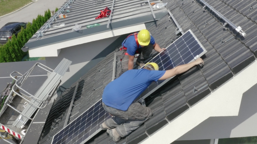 Steady close up drone shot of two workers adding solar panels to the roof mounting rails on sunny Summer day | Shutterstock HD Video #1038836246