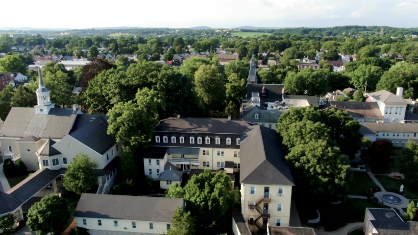 Aerial above church steeple, revealing small town with parade and people lining street in Lititz Pennsylvania
