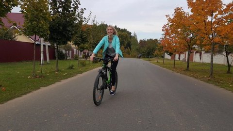woman on a bicycle rides on a country road in autumn, smiling.