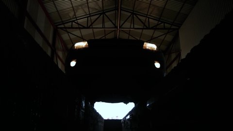 silhouette of sport car with yellow bright headlights driving on pit stop in large garage hangar for maintenance