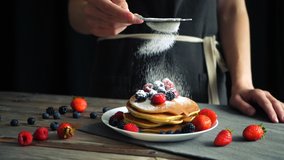 Sugar powder being poured over pancakes beautifully served with berries. Food art. Dessert and breakfast concept. Closeup shot. pastry pour sugar. Seamless cinemagraph video