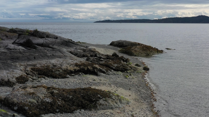 Low aerial view over inlet, ocean and island with boat and mountains in beautiful British Columbia. Canada. 4K.