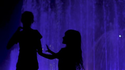 Artistic fountain. Two little girl dance in the night by a colorfull fontain.