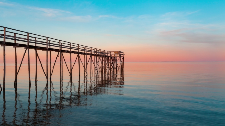 TImelapse of a lake taken near sunset with a pier extending from the beach with its reflection in the water