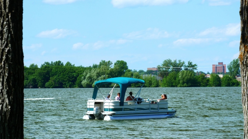 Boating in Minnesota. A Pontoon cruises on beautiful Lake Irving in Bemidji on a sunny day with blue sky and fluffy clouds and the downtown in the background.