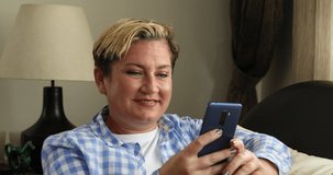 Portrait of a cheerful woman using smartphone to make online video call sitting on couch at home