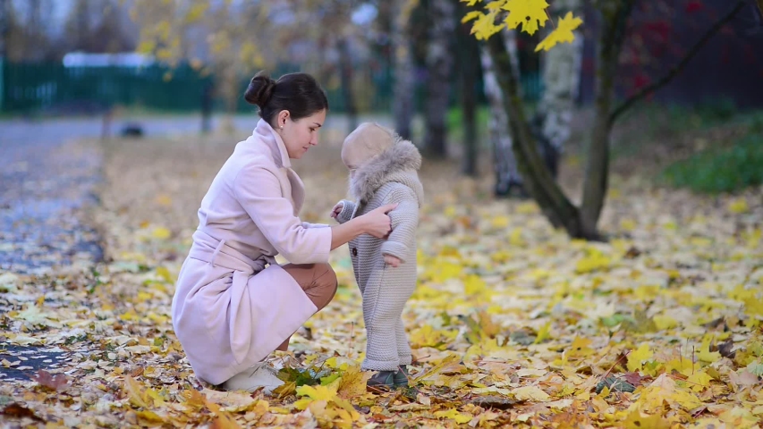 mother carefully fastens clothes to her baby daughter on the street in the autumn evening in the park