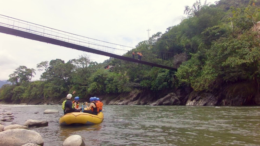 group of tourists in a rafting boat waiting for their teammates to jump from a bridge to pastaza river