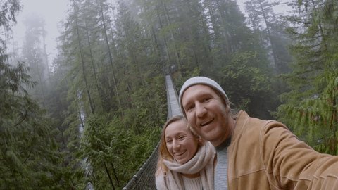 Young couple hiking in pristine forest take cool selfie on a suspended bridge. Canada 