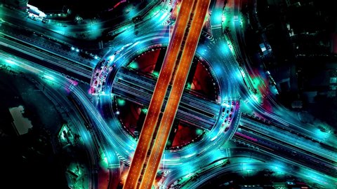 Aerial view of traffic time lapse on intersection circle. Busy traffic at night. Aerial view of road interchange or highway intersection with busy urban traffic speeding on the road at night. Junction