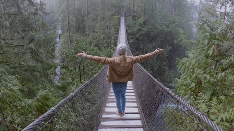 Man stands on suspended bridge in the forest arms wide open 