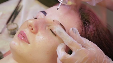The beautician paints the client with an eyebrow with a special brush
