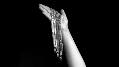 A single female hand comes up and shoes a bunch of payals, anklets, ankle chain, ankle bracelet or ankle string in her hands isolated on black background.

