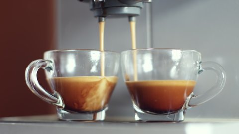 Make coffee. Strong espresso coffee coming out from an automated coffemaker coffe machine and flowing into two glass cups. Beverage drink for breakfast.