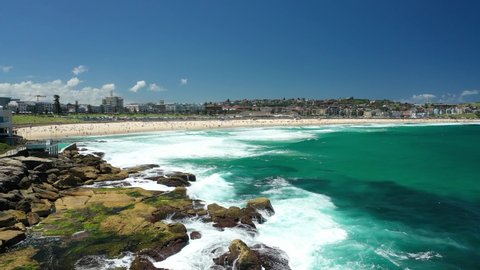 Sydney, Australia. Bondi beach, reveal drone video clip. Beautiful sunny day, big Pacific Ocean waves hitting the rocks. Stunning clear blue ocean water. Most popular white sand beach in Sydney.