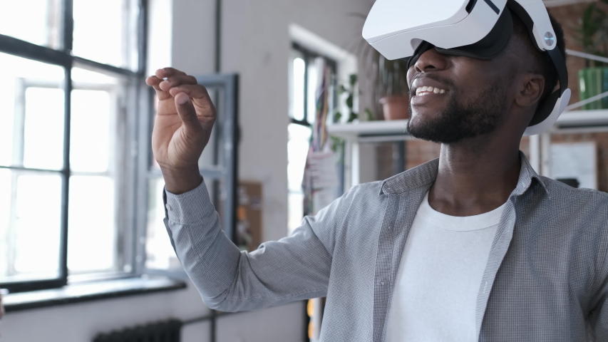 Handsome african american man wearing virtual reality headset. Augmented Reality. Man touch something using modern 3D vr glasses indoors. Student playing using VR glasses on a sunny day. Shot on 4K Royalty-Free Stock Footage #1038922109