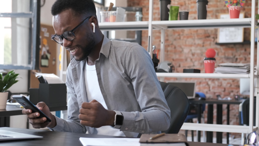 Happy African American man look at smartphone screen overjoyed by great news. Motivated businessman reading excellent online message. Good work result. Emotions of young man from business success. Royalty-Free Stock Footage #1038922139